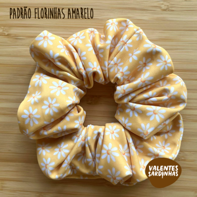 Elástico de cabelo amarelo com padrão de flores brancas sobre fundo de madeira