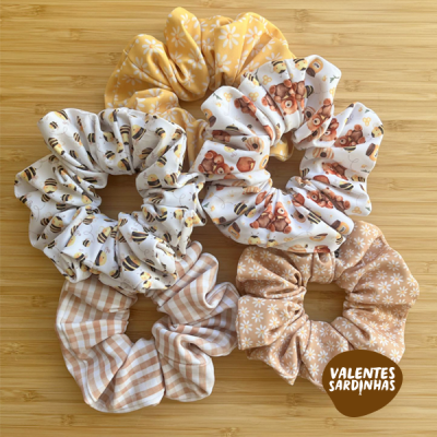 Quatro scrunchies de tecido com diferentes padrões coloridos sobre fundo de madeira clara