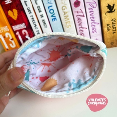 Bolsa pequena de tecido com padrão colorido aberta com livros ao fundo