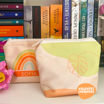 Duas bolsas de tecido com fecho e padrões coloridos em frente a livros