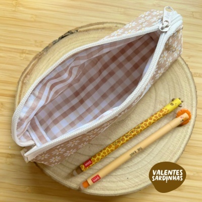 Estojo bege com flores brancas e lápis decorativos sobre base de madeira