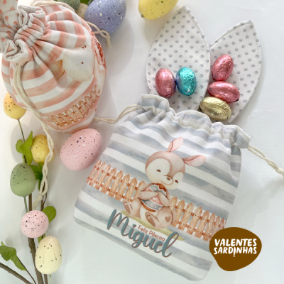 Bolsas de pano decoradas com coelho e ovos de chocolate, com orelhas de coelho em fundo branco.