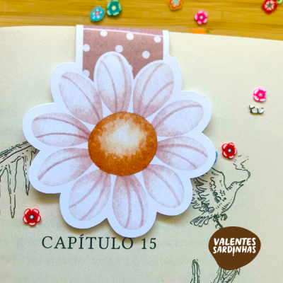 Marcador de livro flor branca com centro castanho sobre página de livro com texto e desenho de ave.