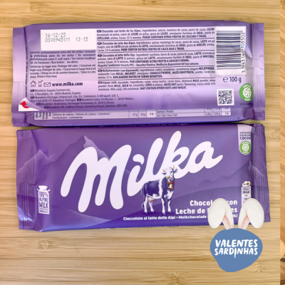 Barra de chocolate Milka em embalagem roxa com informações na parte traseira sobre madeira clara