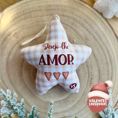 Almofada estrela xadrez bege com texto 'Desejo-lhe AMOR' sobre superfície de madeira clara