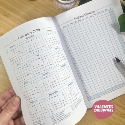 Calendário de bolso aberto de 2026 com calendário e tabela de registos literários sobre mesa de madeira