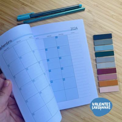 Agenda aberta nas páginas de setembro de 2024, dois marcadores azuis e paleta de amostras de cores sobre mesa de madeira clara.