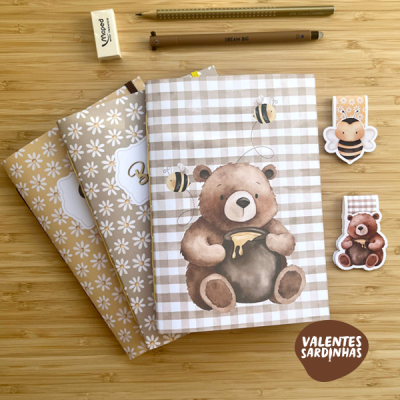 Cadernos com tema de ursinho e abelhas sobre superfície de madeira com lápis, borracha e marcadores
