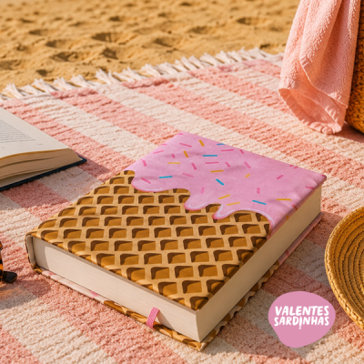 Livro com capa estilo gelado sobre toalha rosa às riscas na praia