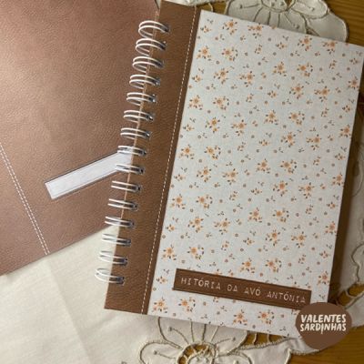 Dois cadernos com lombada espiral; um com padrão floral e título 