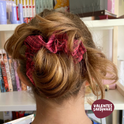 Cabelo loiro preso por scrunchies vermelhos xadrez com fundo de estantes e livros