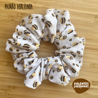 Scrunchie branco com padrão de abelhas pretas e amarelas sobre superfície de madeira