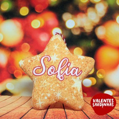 Almofada estrela bege com o nome Sofia em letras cor-de-rosa sobre superfície de madeira e fundo de luzes coloridas