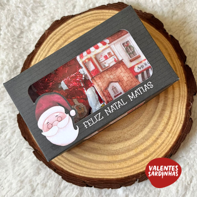 Caixa preta com chocolates embrulhados e ilustração de Pai Natal sobre base de madeira