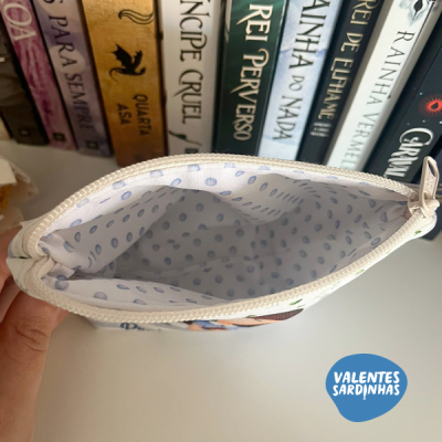 Bolsa pequena branca com interior de pontos azuis aberta em frente a livros.