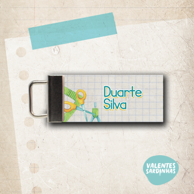 Etiqueta com nome Duarte Silva, imagens de objetos escolares, presilha preta e fundo bege com fita azul