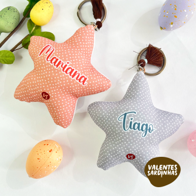 Almofadas em forma de estrela rosa coral e cinza com nomes Mariana e Tiago em texto colorido, com porta-chaves e borlas castanhas.