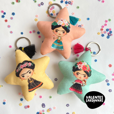 Porta-chaves estrela com personagens femininas coloridas e pompons, fundo branco com pequenas flores coloridas