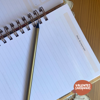 Caderno espiral com lápis dourado sobre mesa de madeira