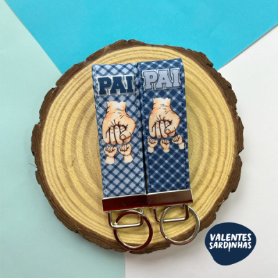 Dois porta-chaves tecido azul com mãos e texto PAI sobre base de madeira