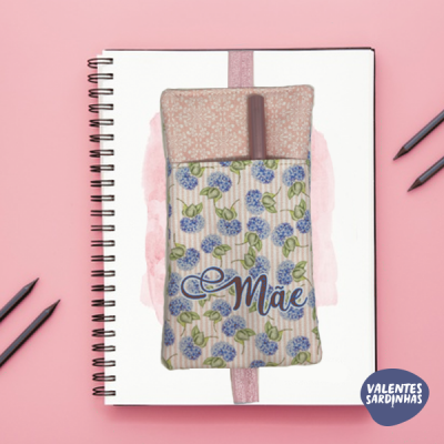 Estojo floral com a palavra Mãe bordada sobre caderno branco espiral em fundo rosa