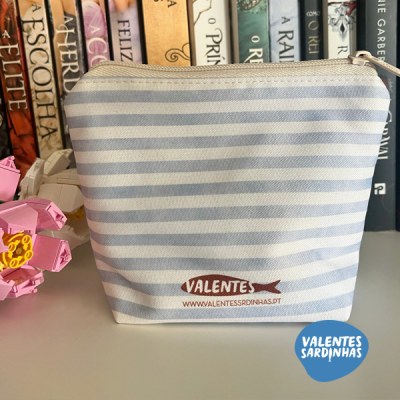 Bolsa riscada azul e branca com logotipo VALENTES e URL, sobre mesa com livros e flor de origami rosa