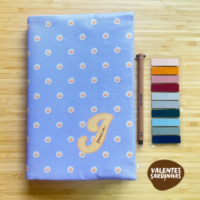 caderno azul com flores e símbolo, caneta castanha, marcadores coloridos, logo Valentes Sardinhas