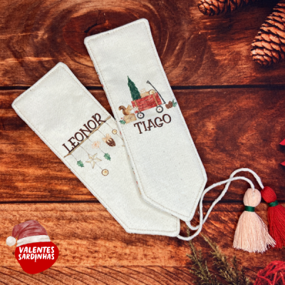Dois marcadores de tecido bordados com nomes e temas natalícios em fundo de madeira