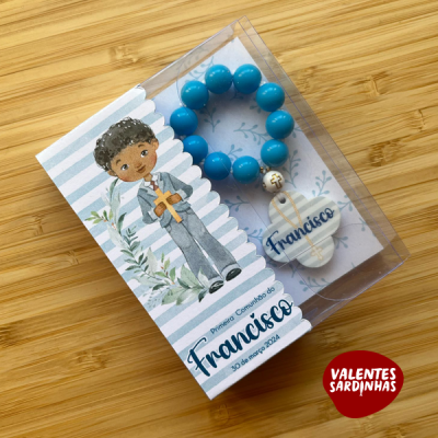 Pulseira azul com crucifixo branco em cartão com ilustração e texto de primeira comunhão