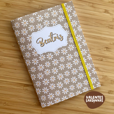 Caderno decorado com padrão de margaridas brancas e nome Beatriz em dourado