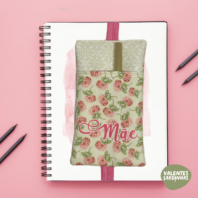 Estojo floral com a palavra 'Mãe' sobre caderno branco de argolas e superfície rosa.