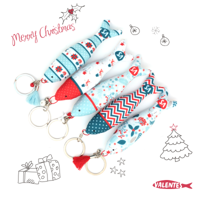 Cinco porta-chaves de tecido em forma de peixe com padrões natalícios coloridos em azul, vermelho e branco.