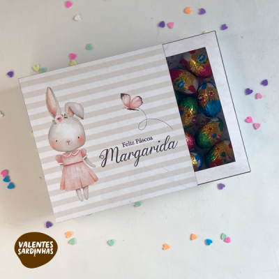 Caixa de chocolates de Páscoa com coelha em roupa rosa e ovos de chocolate coloridos visíveis