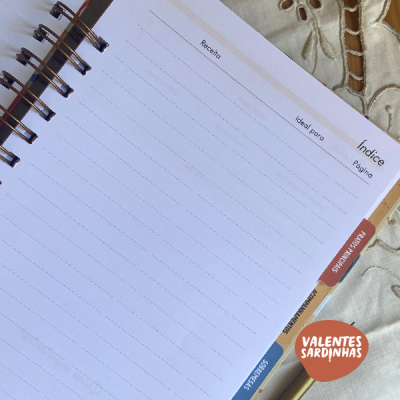 Página de caderno espiral com colunas e separadores coloridos sobre tecido bordado