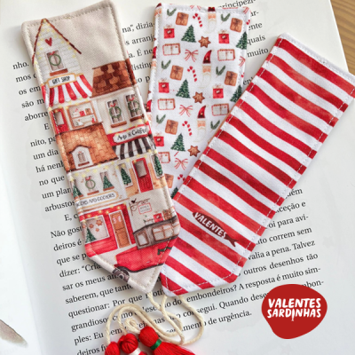 Três marcadores de livros de tecido com diferentes padrões e cores sobre página de livro aberta.