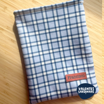 Capa xadrez azul e branco com etiqueta de couro 'Francisco' sobre madeira.
