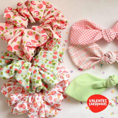 Scrunchies e laços de cabelo com padrões de morangos e quadrados coloridos sobre fundo branco com confetes