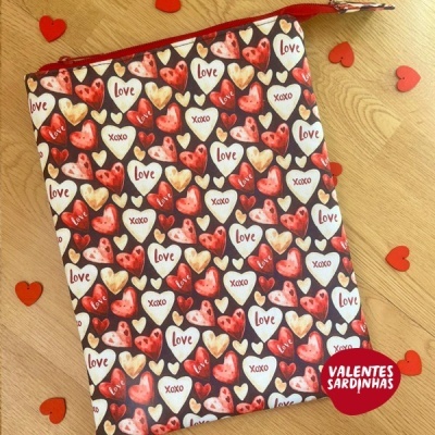 Bolsa de pano com padrão de corações e palavras 'love' e 'xoxo', com fecho vermelho, sobre fundo de madeira clara