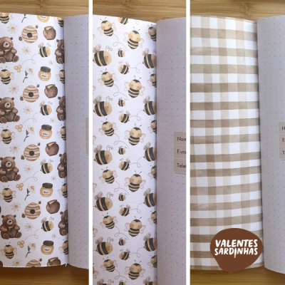 Três folhas de papel decorativo com padrões de ursos e colmeias, abelhas e padrão xadrez, sobre mesa de madeira