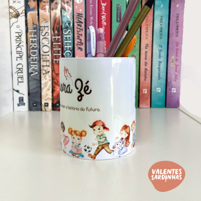 Caneca branca com ilustração de crianças e texto, com canetas dentro, numa estante com livros.