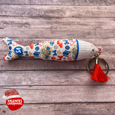 Chaveiro em forma de sardinha colorida com anel metálico e tassel vermelho em fundo de madeira