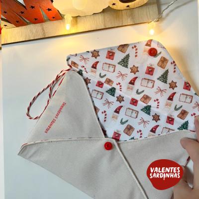 Envelope ou bolsa de tecido com padrão natalício e botão vermelho em superfície branca com luzes