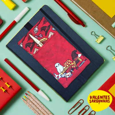 Caderno azul com bolso vermelho decorado com animais e caneta dourada, rodeado de material de papelaria colorido.