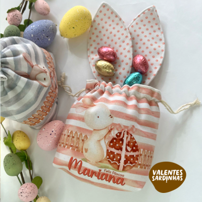 Saco de tecido rosa com coelho, textos de Páscoa e orelhas de coelho, decorado com ovos de chocolate e ovos coloridos