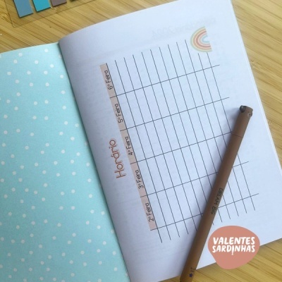 Livro aberto com calendário semanal e caneta castanha sobre mesa de madeira clara