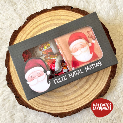 Embalagem preta com chocolates decorados com Pai Natal e texto FELIZ NATAL MATIAS sobre base de madeira