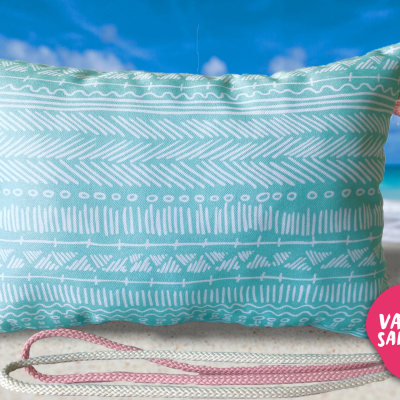Almofada azul claro com padrão branco geométrico e alça de corda na praia