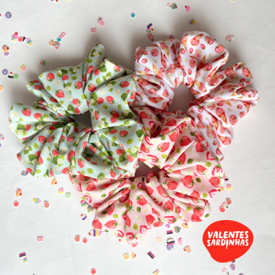 Três scrunchies coloridos com padrão de morangos e confetis coloridos ao redor