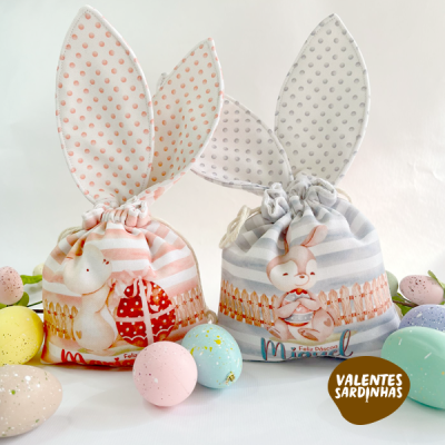 Sacquinhos de tecido com orelhas de coelho e ilustrações de coelhos, rodeados por ovos coloridos.