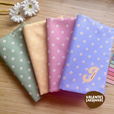 Quatro agendas coloridas com padrão de flores pequenas em tecido e flores brancas ao lado